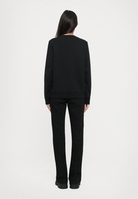 Schwarzer Pullover und schwarze Hose, beide aus weichem Stoff gefertigt. Der Pullover hat einen klassischen Rundhalsausschnitt und eine lockere Passform.