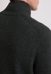 Pull en turtleneck côtelé gris foncé avec un col haut, présentant un tissu tricoté texturé et des coutures d'épaule visibles de l'arrière.