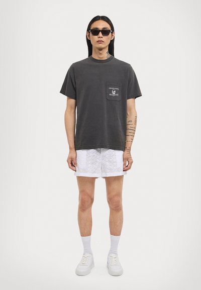 Dark gray cotton t-shirt with a pocket featuring white text and a graphic. Paired with white eyelet shorts and white sneakers.