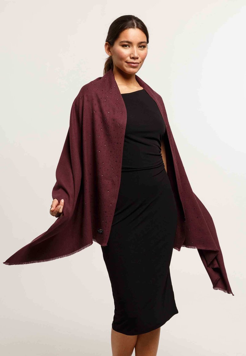 Châle bordeaux avec des accents scintillants subtils, fabriqué à partir d'un tissu doux, présentant un bord frangé et un design drapé sur une robe noire ajustée.
