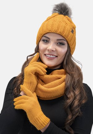 Mustard yellow knitted beanie with a faux fur pom-pom, matching gloves, and a looped scarf. Textured fabric with ribbed accents.