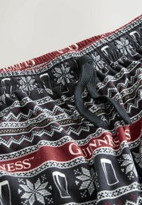 Czarne szorty z tkaniny z czerwonym paskiem w talii, z zimowym wzorem przedstawiającym płatki śniegu i kufle piwa. Zawierają regulowany sznurek.