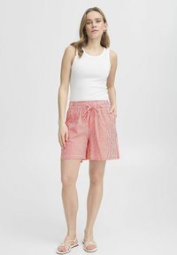 Pantaloni corti a strisce rosse e bianche con vita elastica e coulisse. Abbinati a una canotta bianca e sandali bassi. Tessuto leggero.