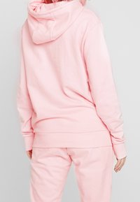 Pink hooded sweatshirt made of soft fabric, featuring a relaxed fit, ribbed cuffs and hem, and a spacious hood. Worn with matching pants.