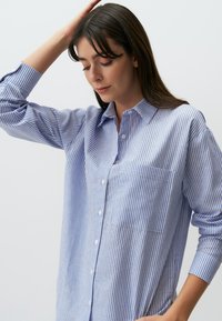 Blauw-wit gestreepte overhemd met lange mouwen, een kraag en een borstzak; katoenen stof met een gladde textuur.
