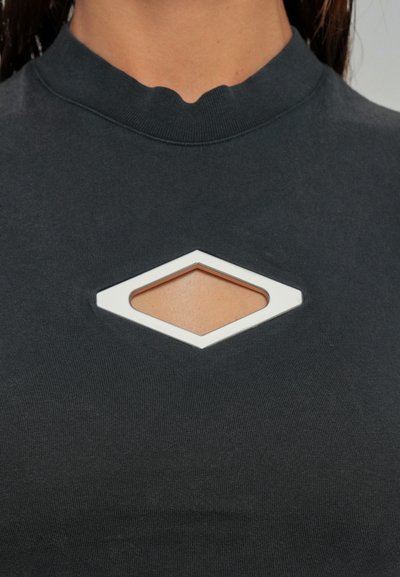 Donna che indossa un top grigio scuro con un piccolo taglio a forma di diamante sul petto che rivela la pelle sottostante.