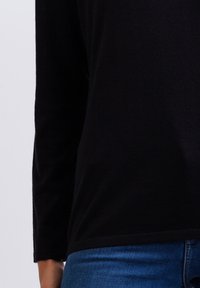 Schwarzes Langarm-Oberteil aus weichem Stoff, mit lockerer Passform und Rundhalsausschnitt, kombiniert mit blauen, eng anliegenden Jeans.