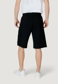 Shorts sportivi neri con vita elastica, dotati di tasche laterali e dettagli testurizzati, abbinati a sneakers bianche.