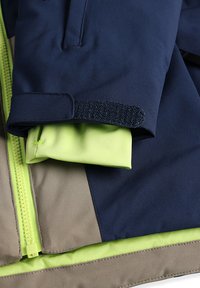 Veste marine et vert lime avec une couche intérieure douce, dotée d'une fermeture éclair, de poignets en Velcro et d'accents beige au niveau de l'ourlet.