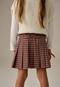 Gonna plissettata in gingham marrone e blu navy con vita, abbinata a un top in maglia color crema. Il tessuto ha una consistenza morbida e presenta dettagli di cucitura visibili.