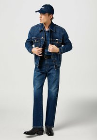 Tummansinisestä denimmistä takista ja farkuista koostuva asu, joka on yhdistetty yhteensopivaan denimmipaitaan ja laivastonsiniseen lippikseen. Mustat nahkasaappaat viimeistelevät asun.