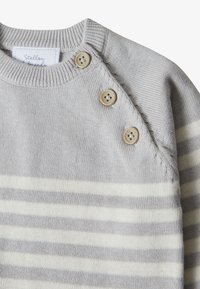 Helles graues gestricktes Sweatshirt mit weißen Streifen. Verfügt über drei beigefarbene Knöpfe an der linken Schulter und einem gerippten Ausschnitt. Weiche Textur.