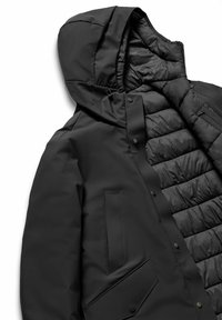 Giacca imbottita nera con cappuccio, caratterizzata da un esterno opaco, un interno trapuntato, chiusure a bottoni a pressione e tasche inclinate. Texture complessivamente liscia.