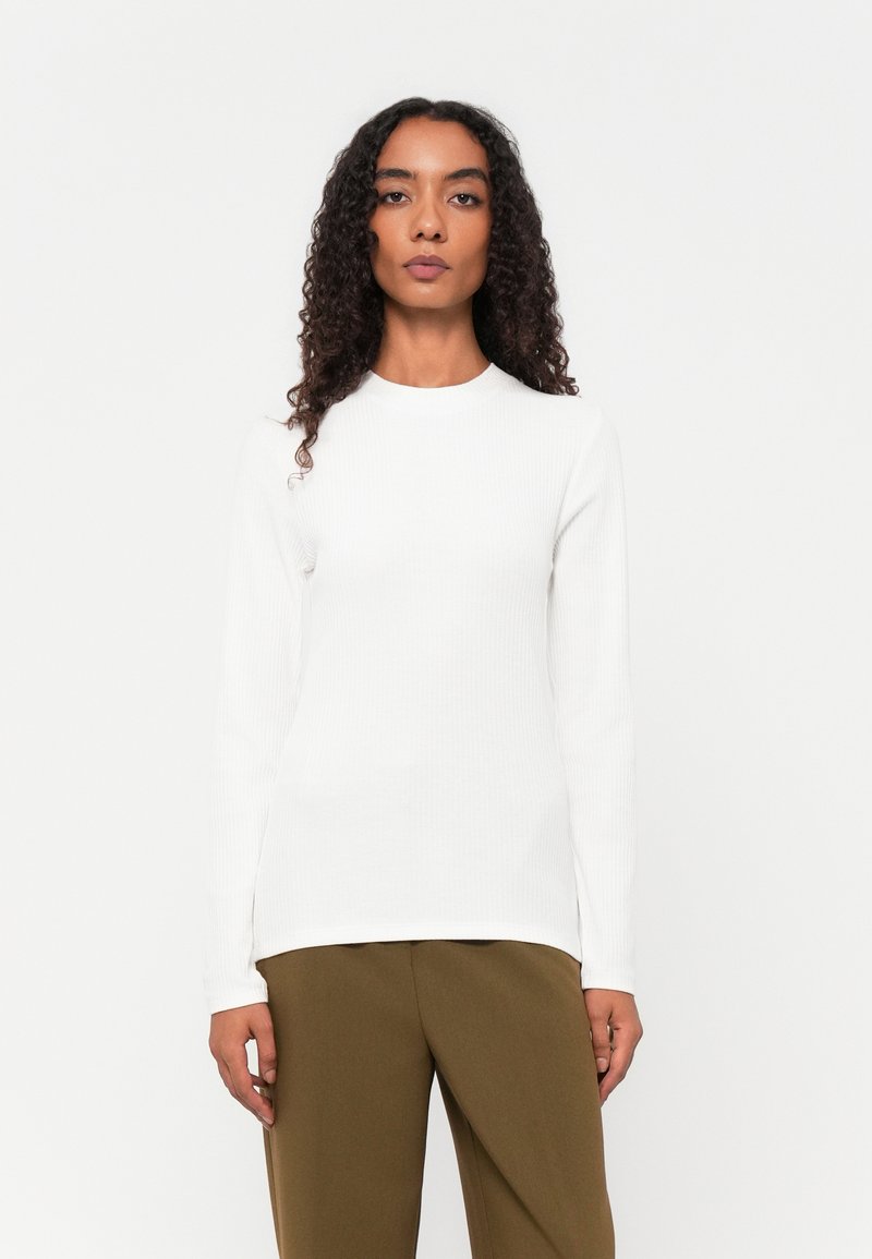 Hvit ribbet langermet topp med rund hals, kombinert med brune vide bukser. Minimalistisk design og jevn tekstur.