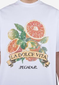 Weißes Baumwoll-T-Shirt mit einem bunten Aufdruck von Zitrusfrüchten und grünen Blättern, darauf der schwarze Text "LA DOLCE VITA" und "PEGADOR".
