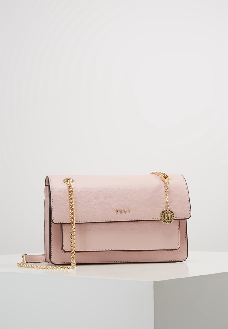 Sac à main rectangulaire rose doux avec bandoulière chaîne dorée, fermeture à rabat et petit pendentif rond doré avec gravure de la marque.