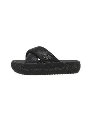 Sandalia negra sin cierre con suela texturizada y amplias correas cruzadas, con un pequeño logo metálico decorativo en el lateral.