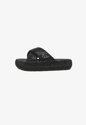 Sandalia negra sin cierre con suela texturizada y amplias correas cruzadas, con un pequeño logo metálico decorativo en el lateral.