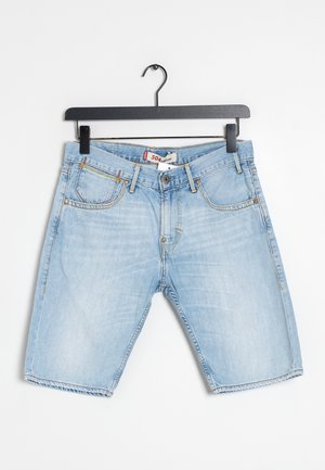 Short en denim bleu clair avec poches avant et passants pour ceinture suspendu sur un cintre noir sur fond blanc.