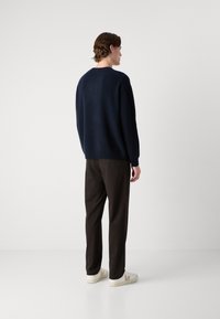 Sötétkék crewneck pulóver, puha anyagból készült, barna nadrággal és fehér sportcipővel párosítva, amelyek világosbarna akcentussal rendelkeznek.