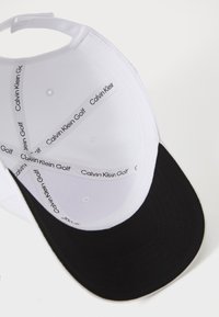 Calvin Klein golfsapka fekete napellenzővel és fehér koronával. Belül textúrált anyag található és nyomtatott márka címkék.