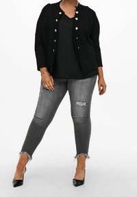 Czarny, teksturowany kardigan z złotymi guzikami, zestawiony z czarną bluzką i poszarpanymi szarymi rurkami. Czarne szpilki dopełniają stylizację.