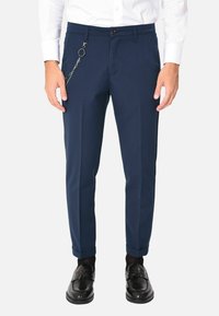 Pantaloni blu navy con una vestibilità slim, dotati di un accentuazione in catena sulla vita, design sartoriale e orli arrotolati. Il materiale appare liscio e leggero.