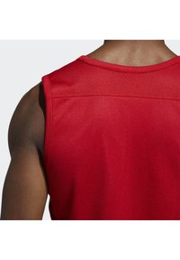 Débardeur de sport rouge avec un tissu en maille respirant, un design sans manches et des coutures renforcées autour de l'encolure et des épaules.