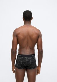 Μαύρα μποξεράκια με μοτίβο λογότυπου, ελαστική μέση και απαλό ύφασμα, παρουσιασμένα σε ανδρικό μοντέλο από πίσω.