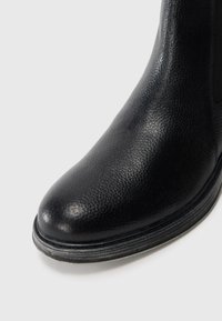 Bottine en cuir noir avec une surface texturée, une pointe arrondie, des détails de couture subtils et un petit talon empilé.