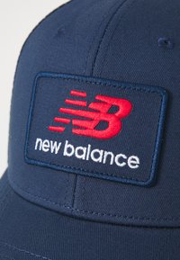 Cappellino da baseball blu navy in cotone con corona strutturata, caratterizzato da un logo ricamato in rosso e bianco etichettato "new balance".