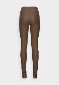 Leggings en simili cuir marron avec une taille haute, une texture lisse et une silhouette ajustée, présentant un design sans couture et des détails de ruché aux chevilles.