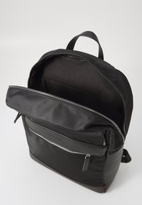 Black backpack made of smooth fabric, featuring a zippered front pocket, a spacious interior, and a loop handle on top.