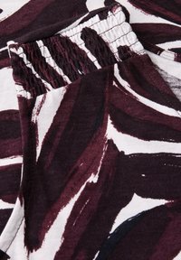 Blommönstrad tyg i djup burgundy och vitt, med elastiska sömmar för komfort. Slät textur med en lätt lyster.