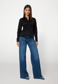 Juodas marškinis su ilgomis rankovėmis, derinamas su mėlynomis plačiomis kelnėmis. Avalynė turi smailius pirštus ir dekoratyvinius akcentus.