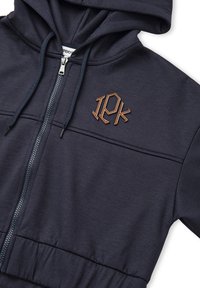 Sudadera con cremallera en color marino, que presenta una capucha con cordón, tejido texturizado y un logo bordado en marrón en el lado izquierdo del pecho.