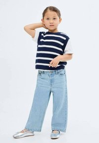 Pulover tricotat cu dungi albastre și albe, purtat peste un tricou alb, asortat cu blugi largi de culoare bleumarin deschis și balerini argintii.