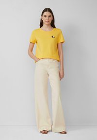 T-shirt en coton jaune avec un col rond et un graphique en noir et blanc sur le devant, associé à un pantalon large beige clair.