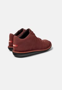 Röda läder skor med en slät yta, låg profil och svart gummisula. Har snörning och en logotypdetalj på baksidan.