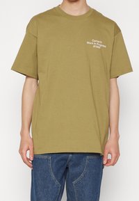 Camiseta de algodón de color verde oliva con mangas cortas, cuello redondo y texto blanco "Carhartt Work In Progress 1989" impreso en el pecho.