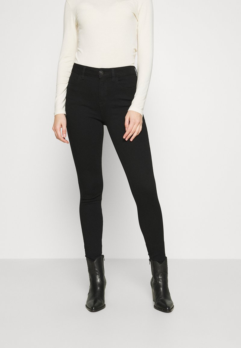 Black skinny jeans with a high waist, made of denim. Paired with a long-sleeve ivory top and black ankle boots. Smooth texture, fitted design.
