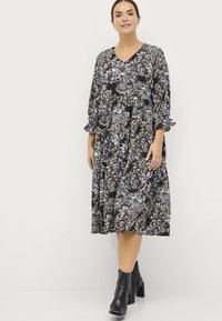 Zwart bloemenjurk met een V-hals, 3/4 mouwen en ruches bij de mouwen. Heeft een gelaagde rok met blauwe, paarse en witte accenten. Gemaakt met zwarte enkellaarzen.