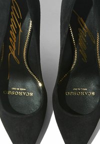 Tacchi alti in suede nero con punte affusolate. Logo dorato sulla soletta e dettagli con cerniera lungo i bordi. Interno in pelle liscia.