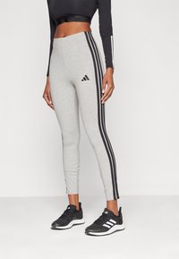 Grå leggings med svart tre-stripesdesign på sidorna, Adidas-logotyp på övre benet, tillverkad av ett stretchigt material för komfort.