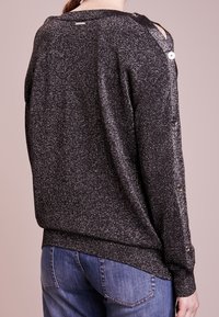 Maglione nero lucido a maglia con accenti di bottoni e design con spalle scoperte, caratterizzato da un orlo a coste e una vestibilità casual. La vista posteriore mostra la texture e i dettagli.