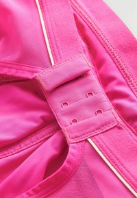 Felle roze sportkleding met een textuur van gaasstof, verstelbare riemhardware en contrasterende stiksels langs de randen.