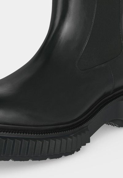 Botte en cuir noir avec panneau latéral élastique et semelle épaisse en caoutchouc rainurée, conçue pour l'adhérence et la durabilité.