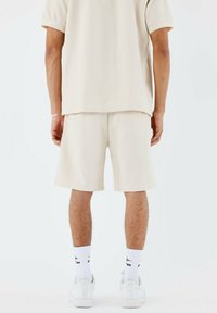 Camisa corta de manga corta texturizada beige y pantalones cortos a juego. Tela de mezcla de algodón con patrones sutiles. Zapatillas blancas y calcetines.