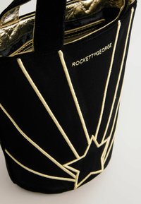 Čierna zamatová taška na rameno s kovovými detailami v zlatej farbe, vyšívaným vzorom hviezd a hviezdicovým dizajnom vyžarujúcim zo spodnej časti.