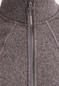 Acercamiento a un suéter de punto gris con una cremallera frontal centrada y cuello alto.
